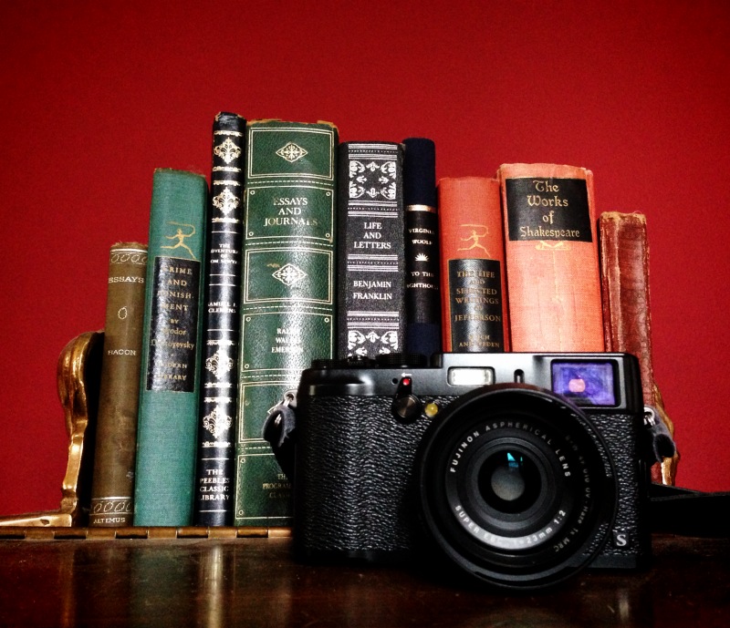 Fuji X100s in front of books. Red background.