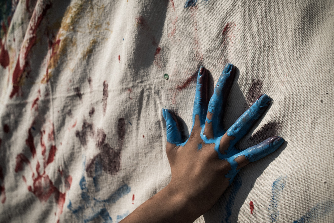 Blue paint on hand. Hand painting white canvas.