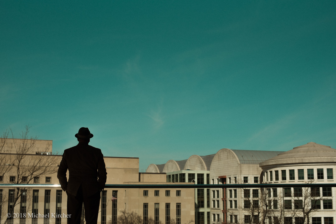 A man in a fedora stands in shadow and takes in the view from the rooftop terrace of the National Gallery of Art, East Building. Washington DC.