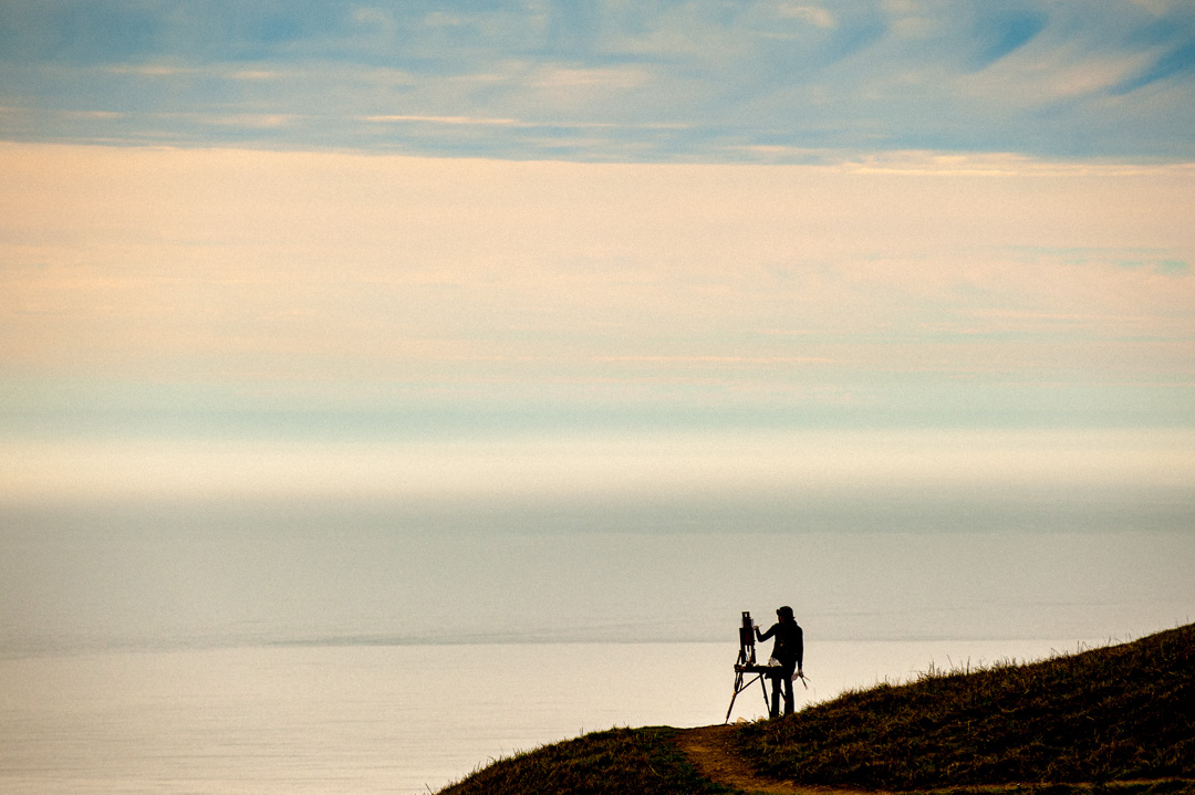 Silhouetted woman with painting easel overlooking the Pacific Ocean.