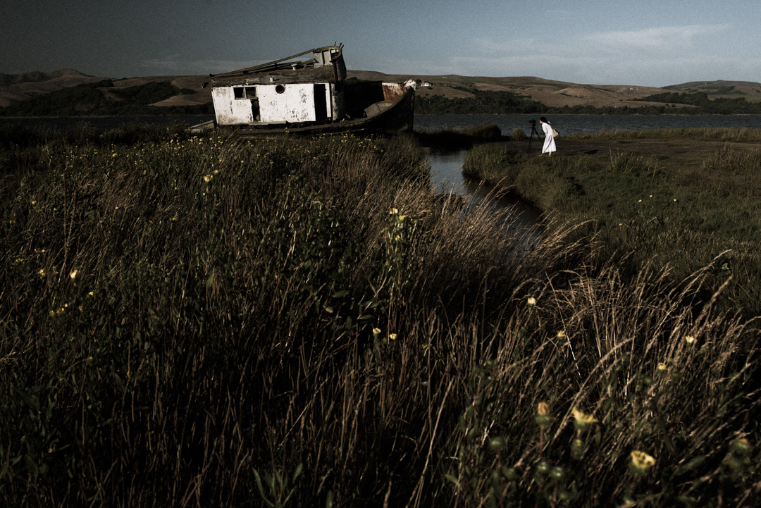 A woman in white dress looks through her camera at the Point Reyes ship wreck on Tomales Bay.